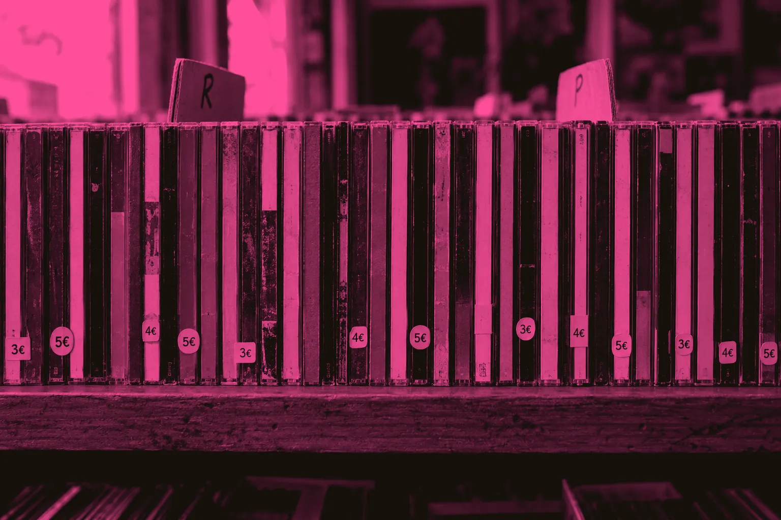 A shelf of used CDs spine-out in a record shop, with price stickers and handwritten section cards.